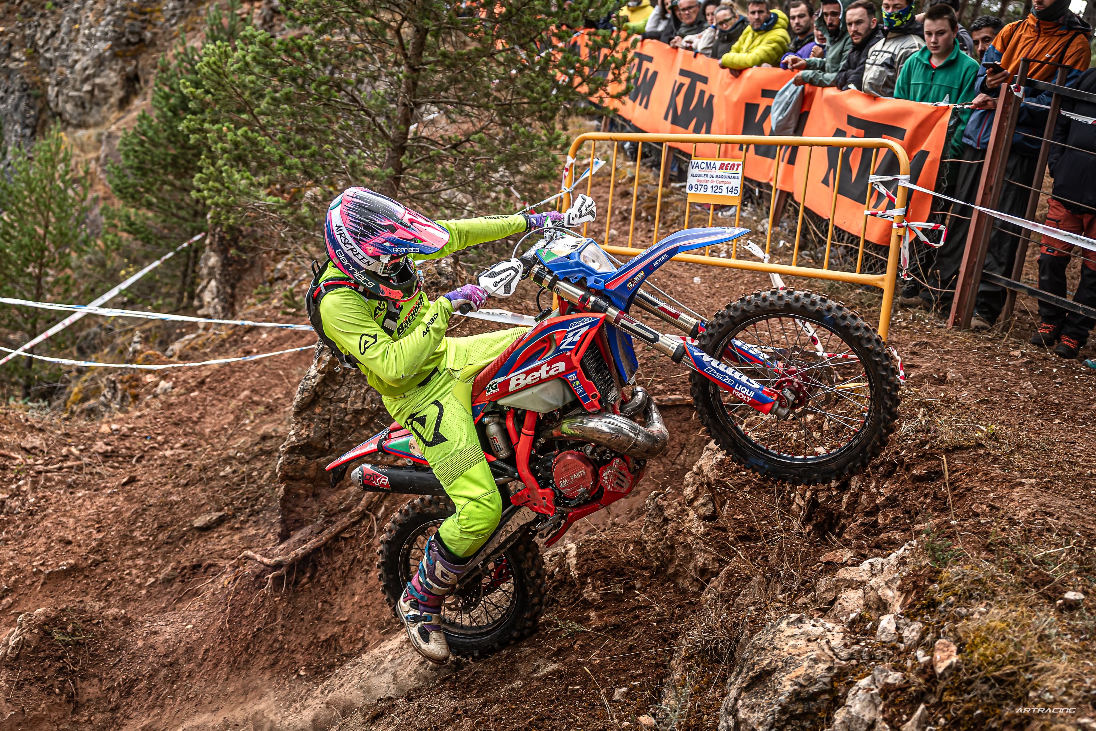 Enduro-Fahrer in neongelber Kleidung erklimmt mit seinem Motorrad einen steilen, felsigen Hang vor begeisterten Zuschauern.