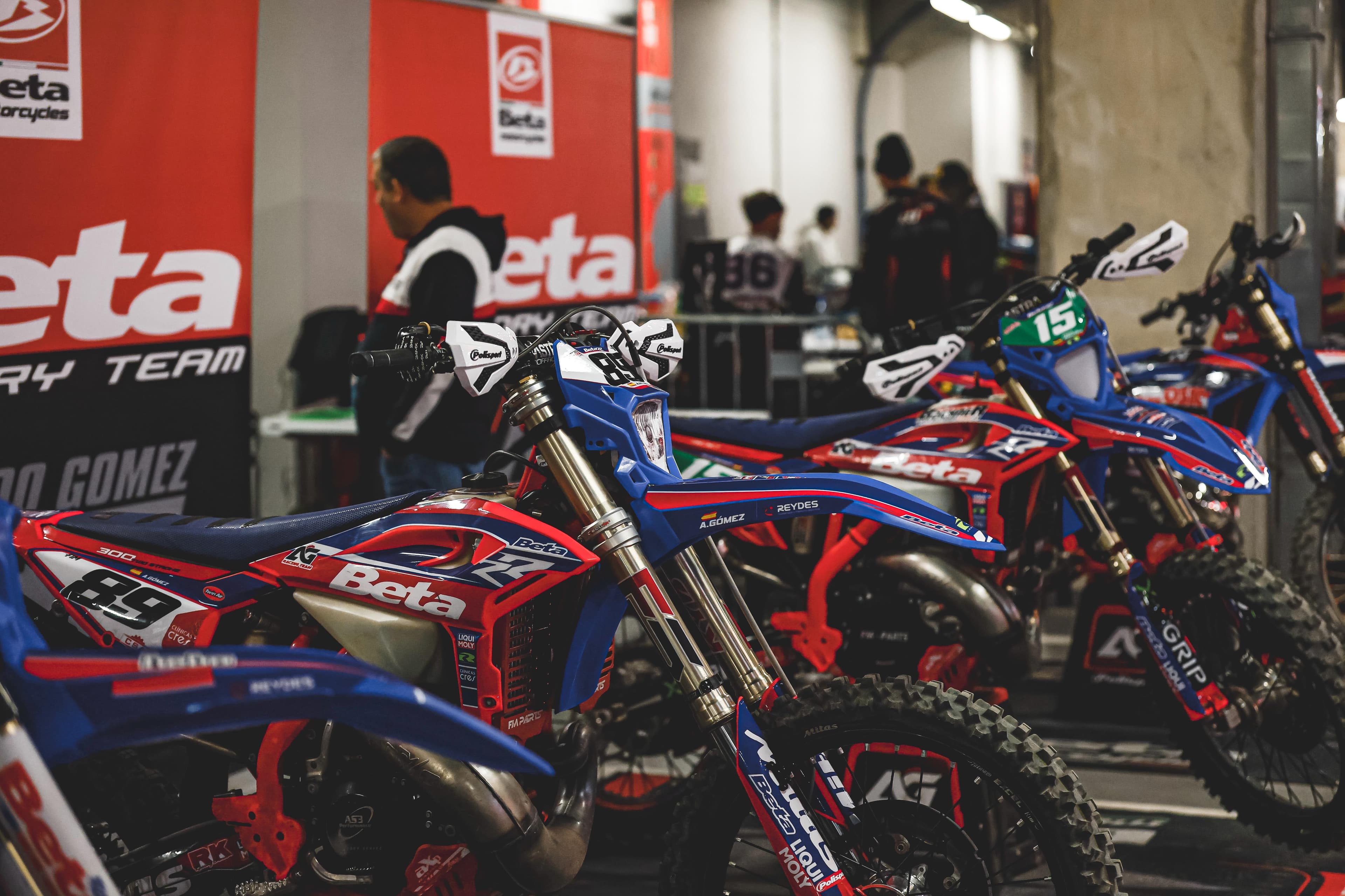 Rote und blaue Beta-Rennmotorräder mit Stollenreifen stehen in einer Reihe vor einem roten Banner.